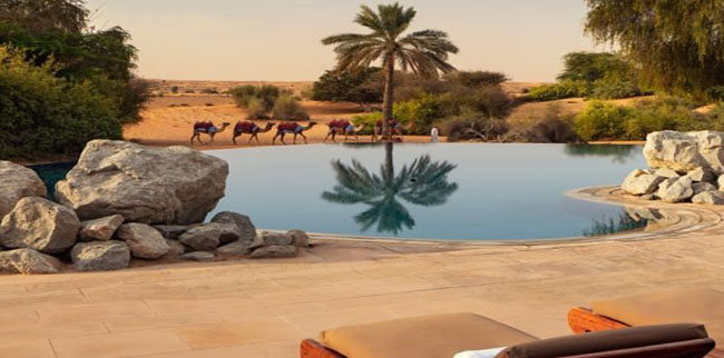 Luxurious Infinity pool at AL Maha Desert Resort sorounded by rocks palms in the desert. Bab Al Shams Desert Dubai